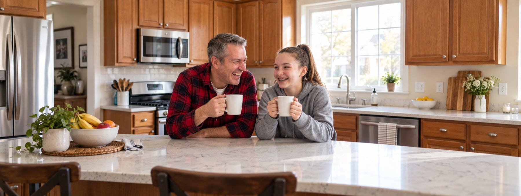 An uncle and his teenage niece laughing over coffee at a kitchen island