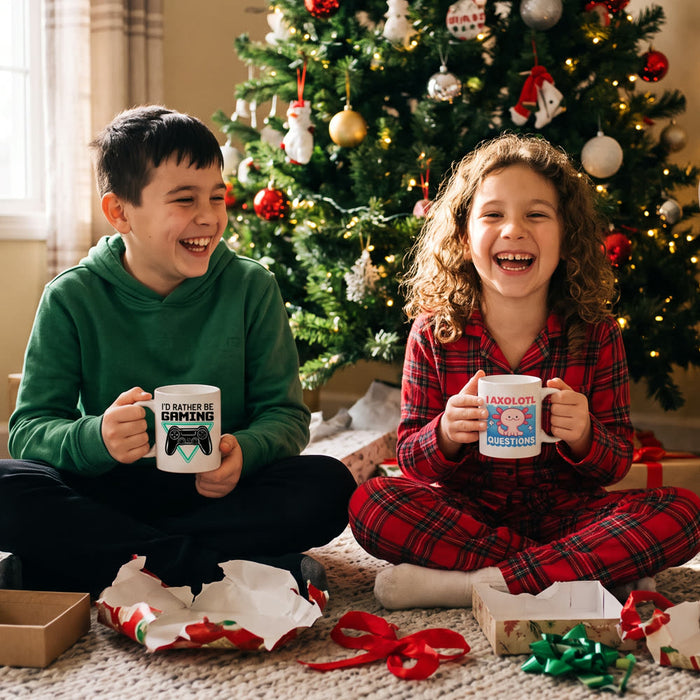 A brother and sister laugh in front of the Christmas tree holding an I'd Rather Be Gaming mug and an I Axolotl Questions mug among torn wrapping paper