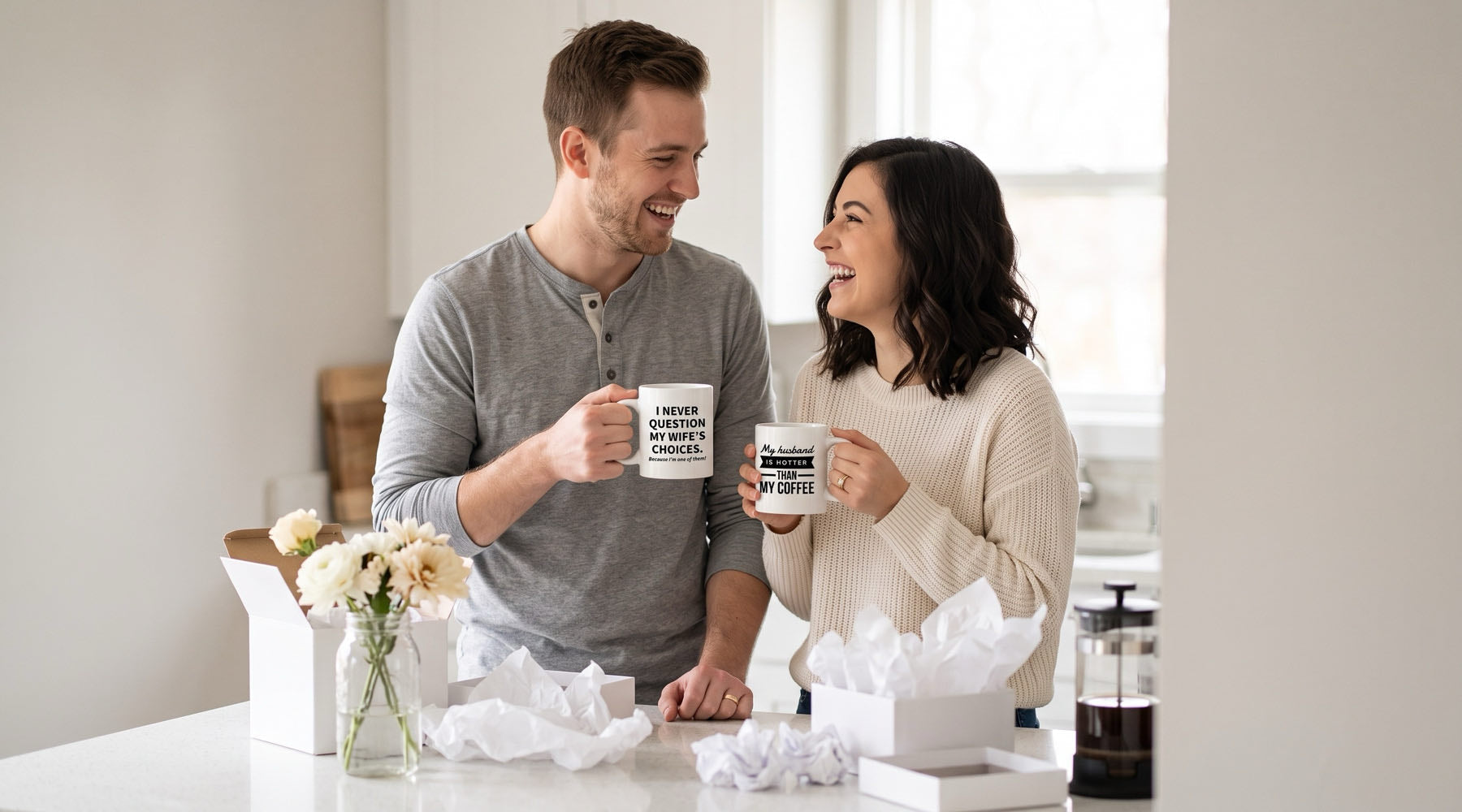 Newlyweds laughing at their kitchen counter with "I never question my wife's choices" and "hotter than my coffee" mugs